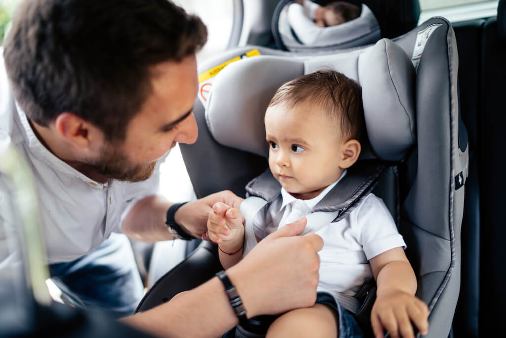 close up portrait of young father securing baby in child seat of car